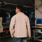 Person wearing a beige jacket and blue jeans in an industrial setting