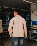 Person wearing a beige jacket and blue jeans in an industrial setting