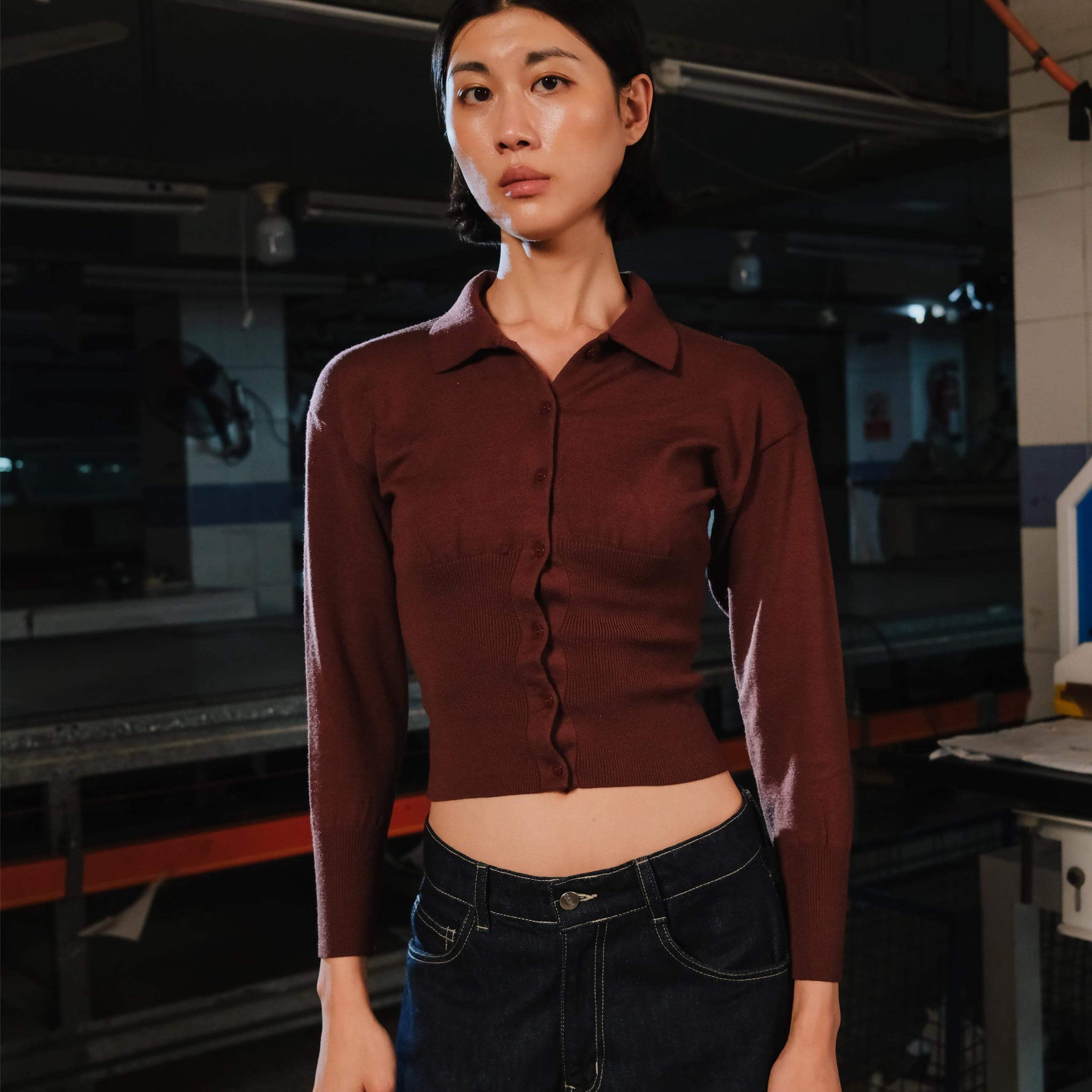 Person wearing a brown shirt and dark jeans in an industrial setting