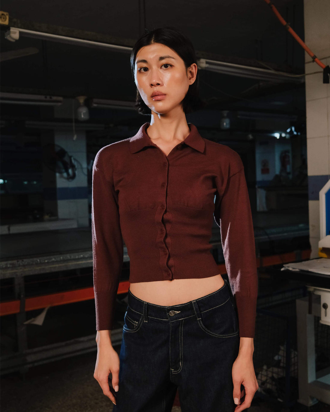 Person wearing a brown shirt and dark jeans in an industrial setting