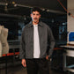 Man wearing a gray jacket over a white shirt in an industrial setting