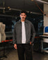 Man wearing a gray jacket over a white shirt in an industrial setting
