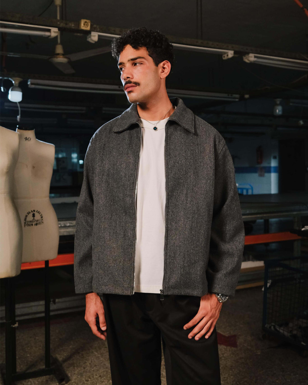 Man wearing a gray jacket over a white shirt in an indoor setting with mannequins and equipment.