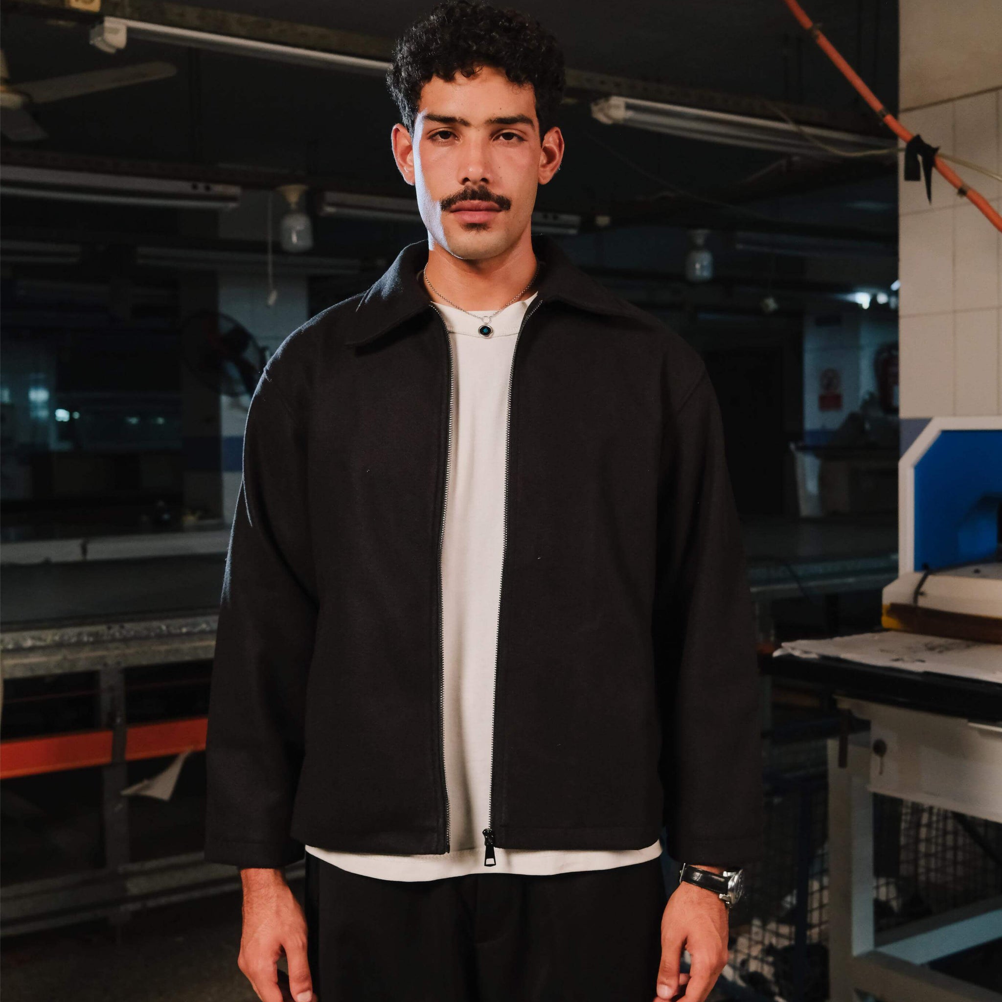 Man wearing a black jacket and white shirt in an industrial setting