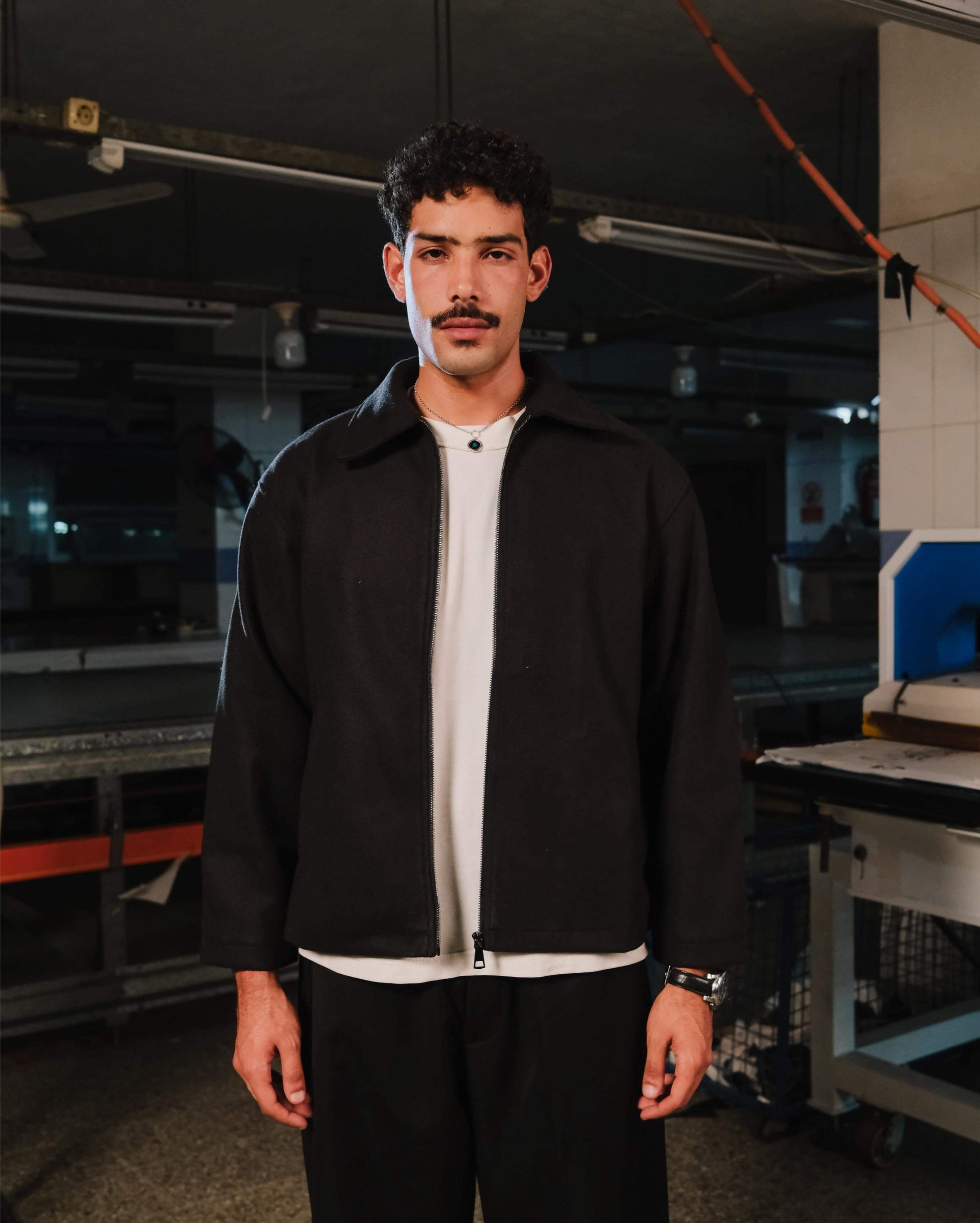 Man wearing a black jacket and white shirt in an industrial setting
