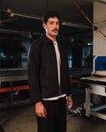 Man wearing a black jacket and white shirt in an industrial setting