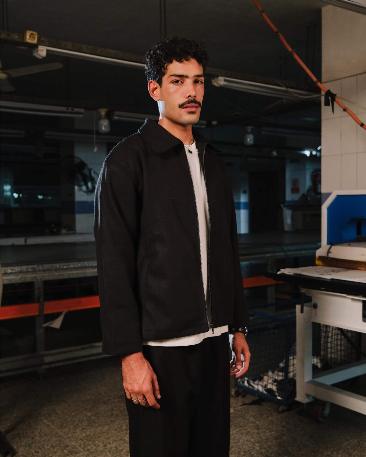Man wearing a black jacket and white shirt in an industrial setting