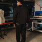 Person wearing a black outfit in a workshop setting with machinery and equipment.