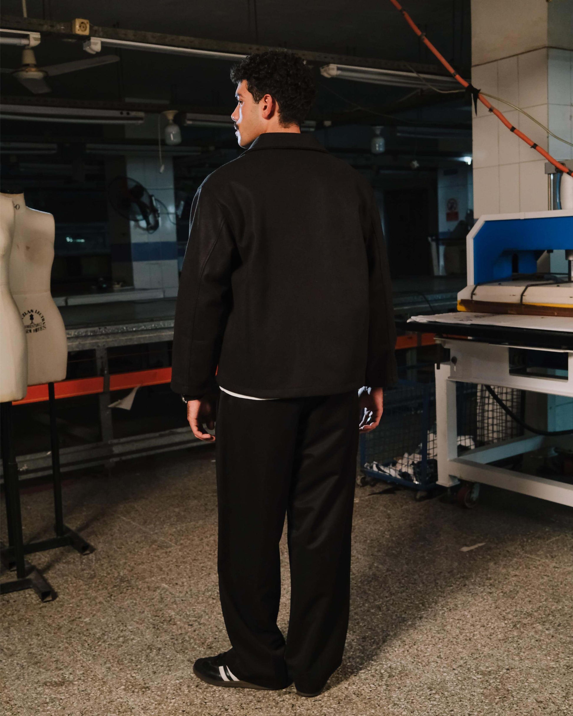 Person wearing a black outfit in a workshop setting with machinery and equipment.