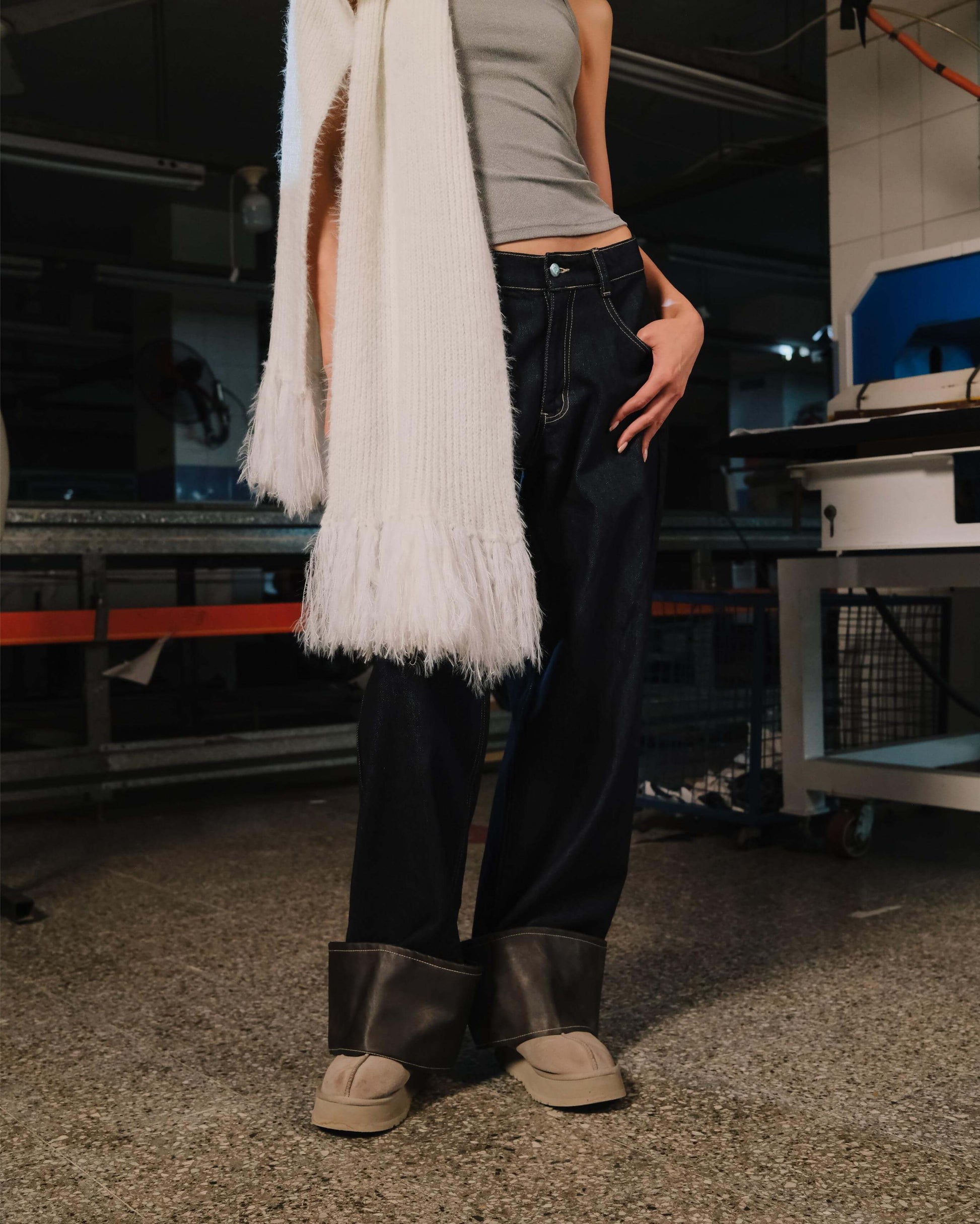 Person wearing a white scarf, gray top, black pants, and beige shoes in an indoor setting.