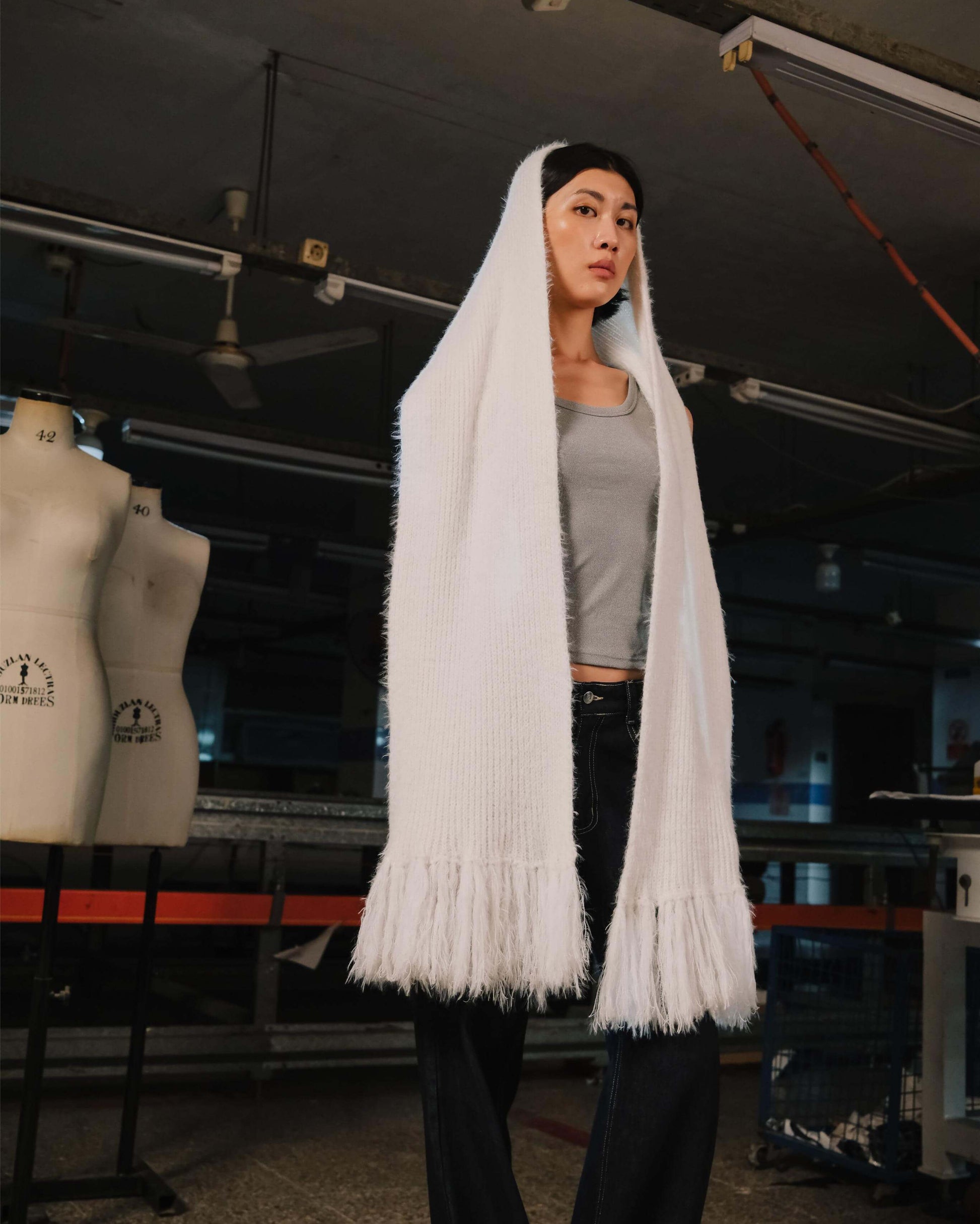 Person wearing a long white scarf in an indoor setting with mannequins in the background