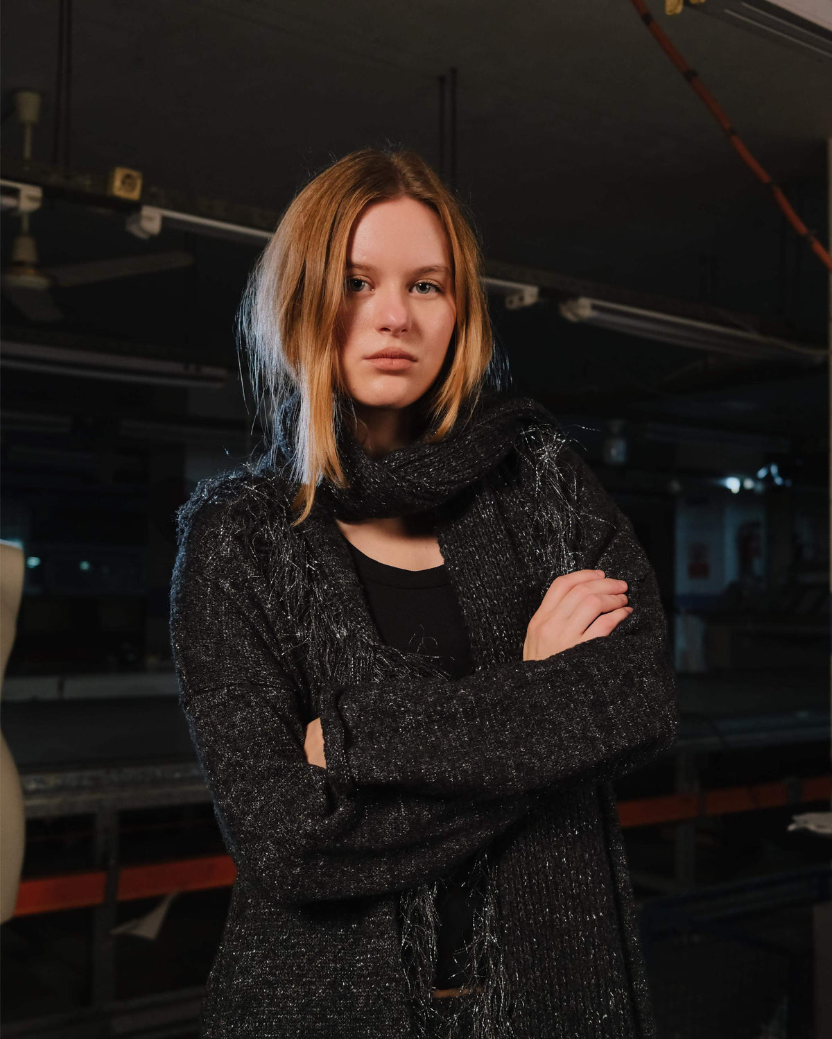 Person wearing a dark textured coat with arms crossed in an indoor setting