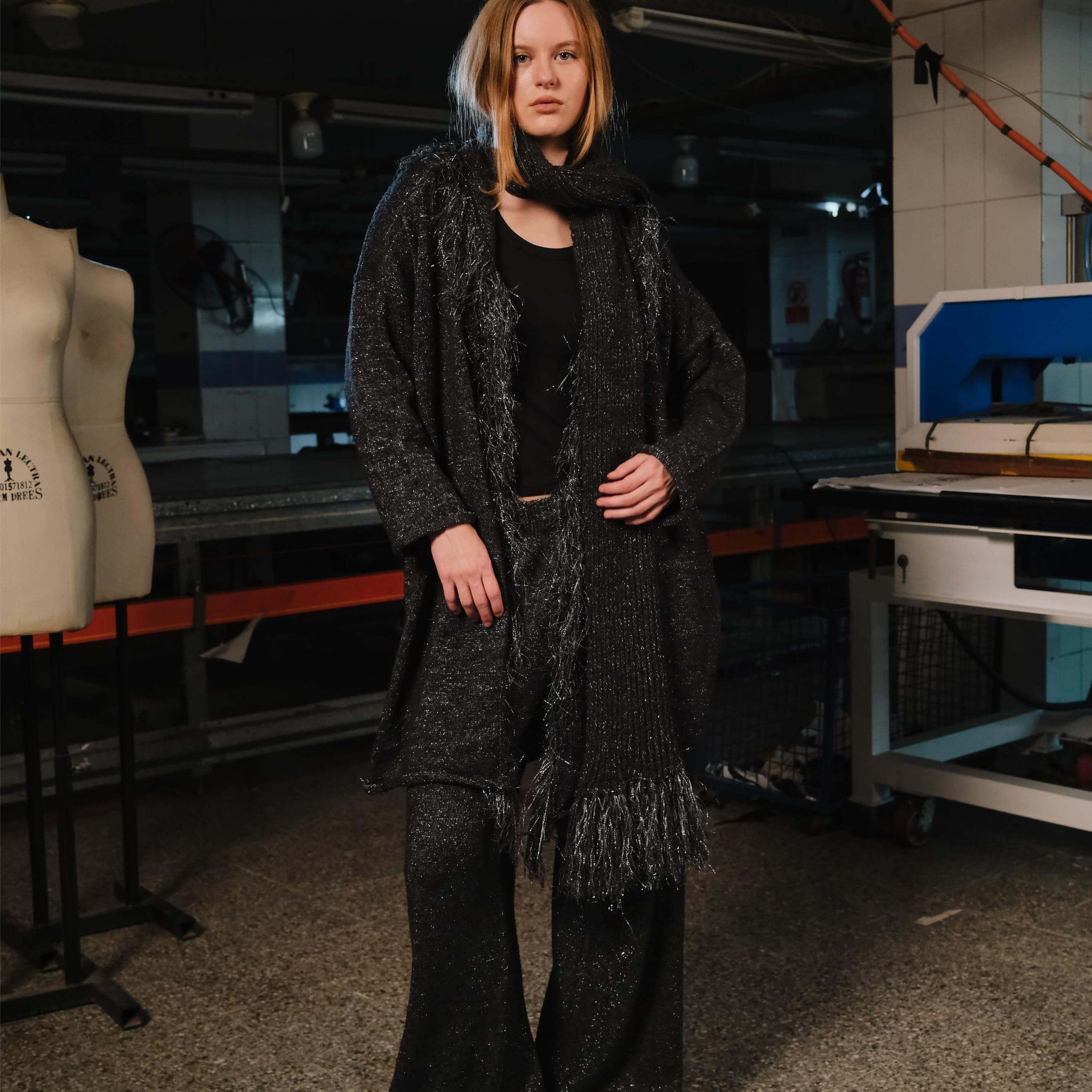 Person wearing a dark coat and scarf in an indoor setting with equipment in the background