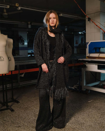 Person wearing a dark coat and scarf in an indoor setting with equipment in the background