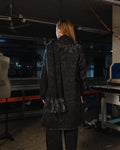 Person wearing a dark coat with sequin details in an indoor setting