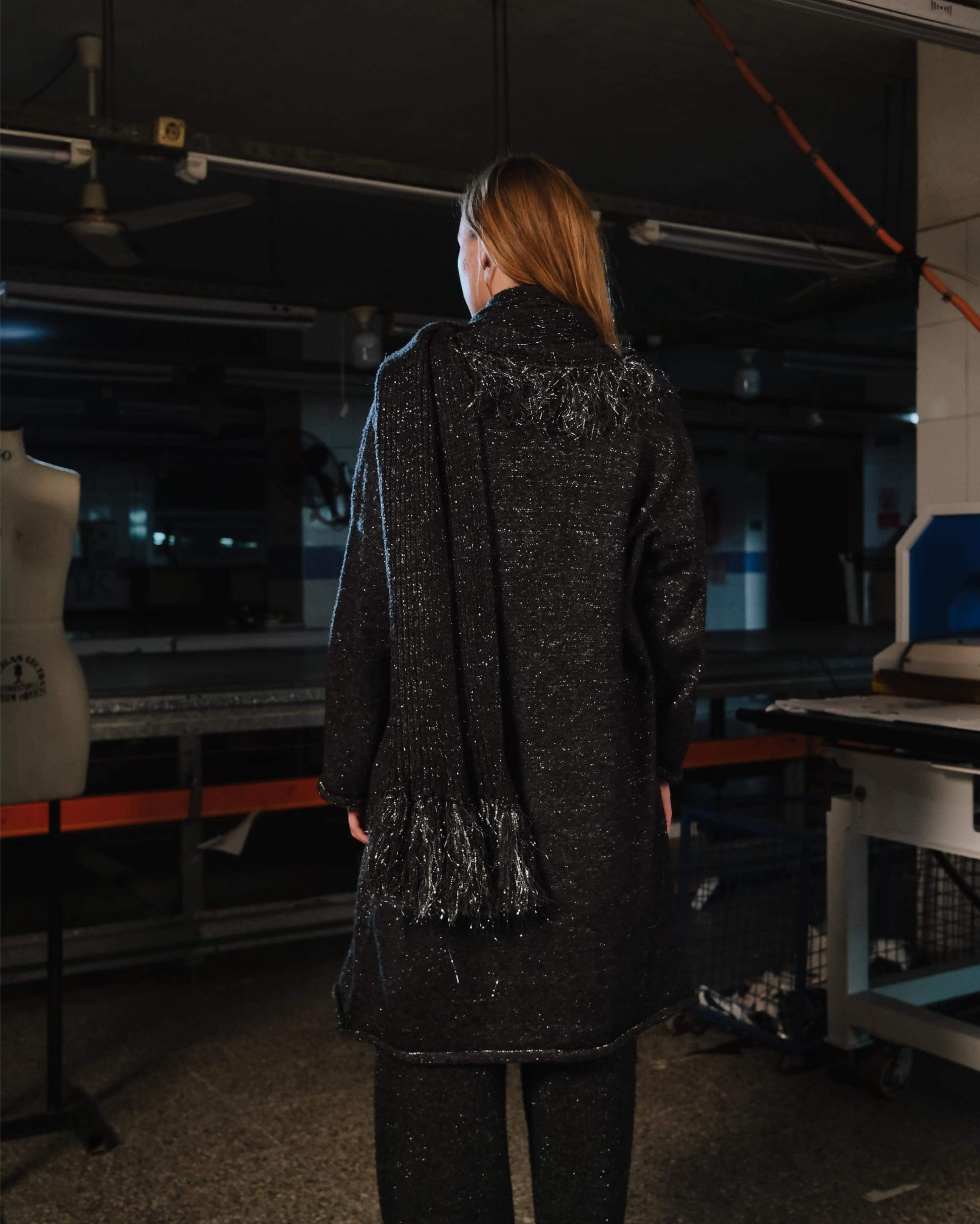 Person wearing a dark coat with sequin details in an indoor setting