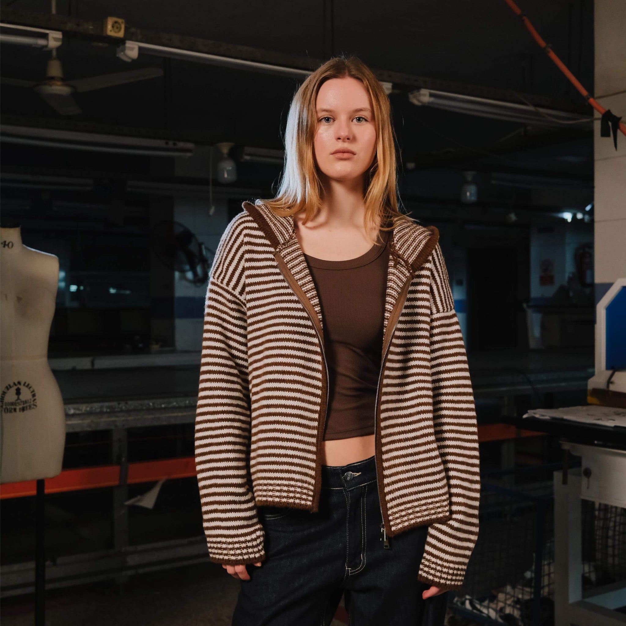 Person wearing a striped sweater in an indoor setting with equipment and a mannequin in the background