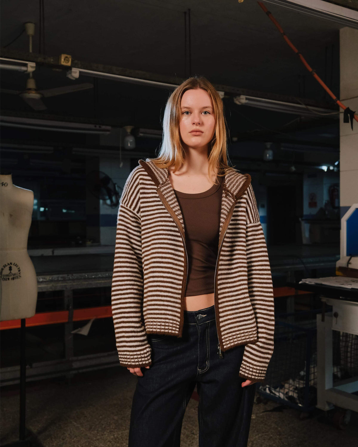 Person wearing a striped sweater in an indoor setting with equipment and a mannequin in the background