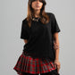Person wearing a black t-shirt with a red plaid skirt on a gray background