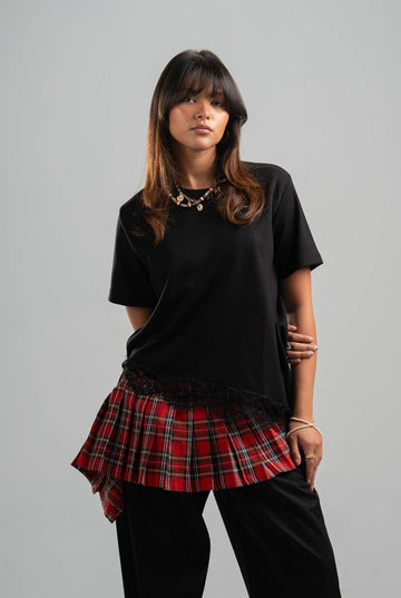 Person wearing a black t-shirt with a red plaid skirt on a gray background