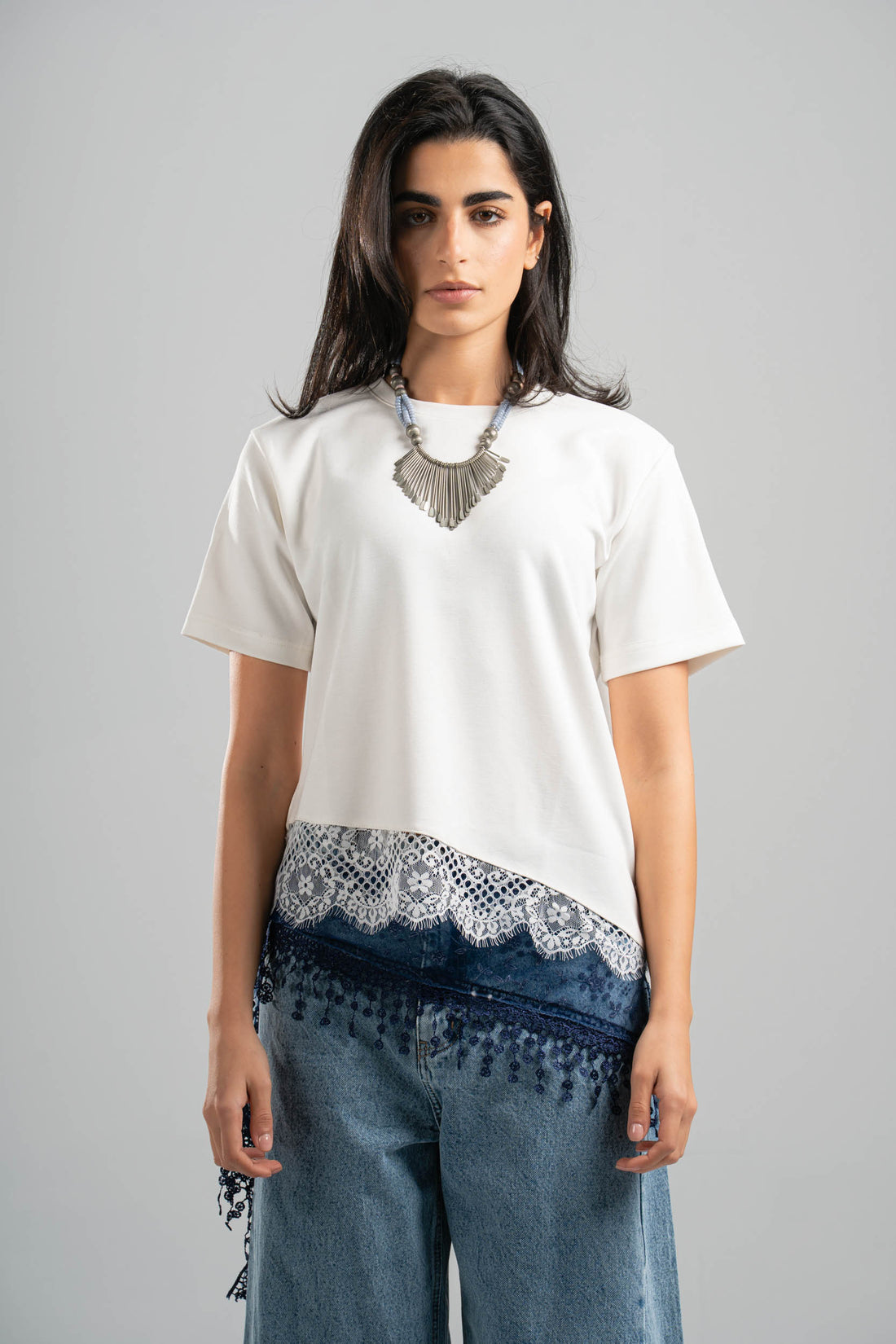 Woman wearing a white top with lace details and blue jeans on a gray background