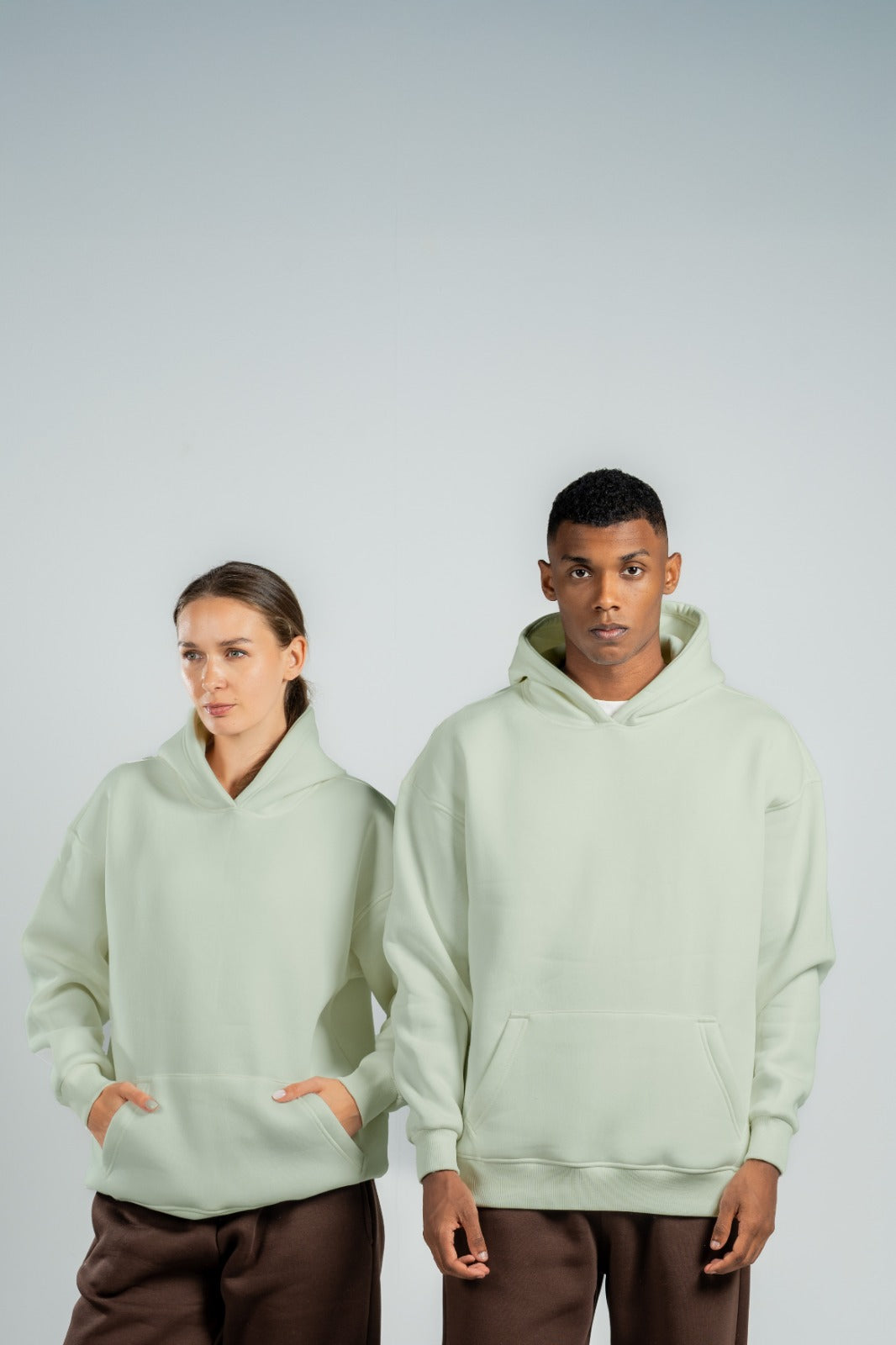 Two people wearing mint green hoodies on a plain background