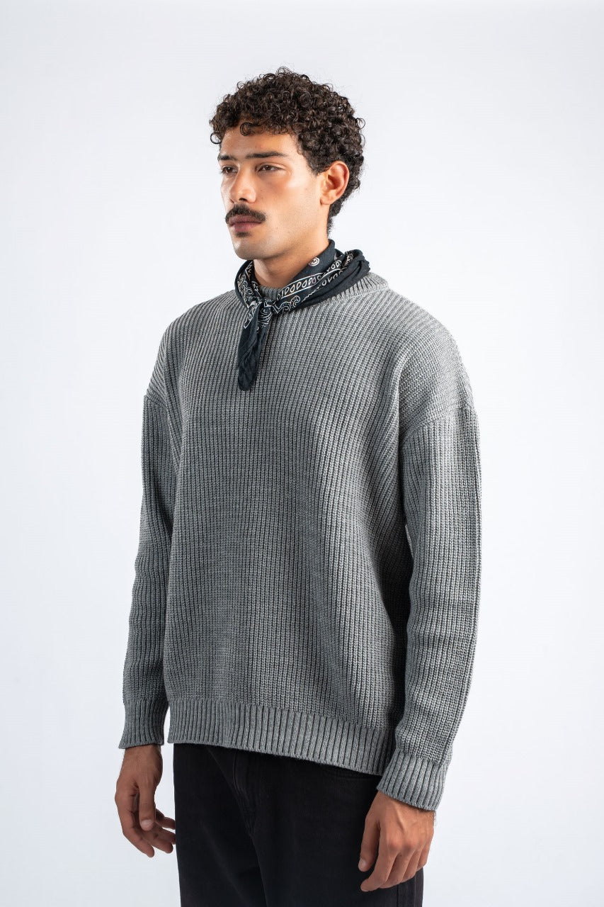 Man wearing a gray sweater with a black scarf around his neck on a white background