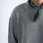 Person wearing a gray ribbed sweater with a black bandana around the neck on a light gray background