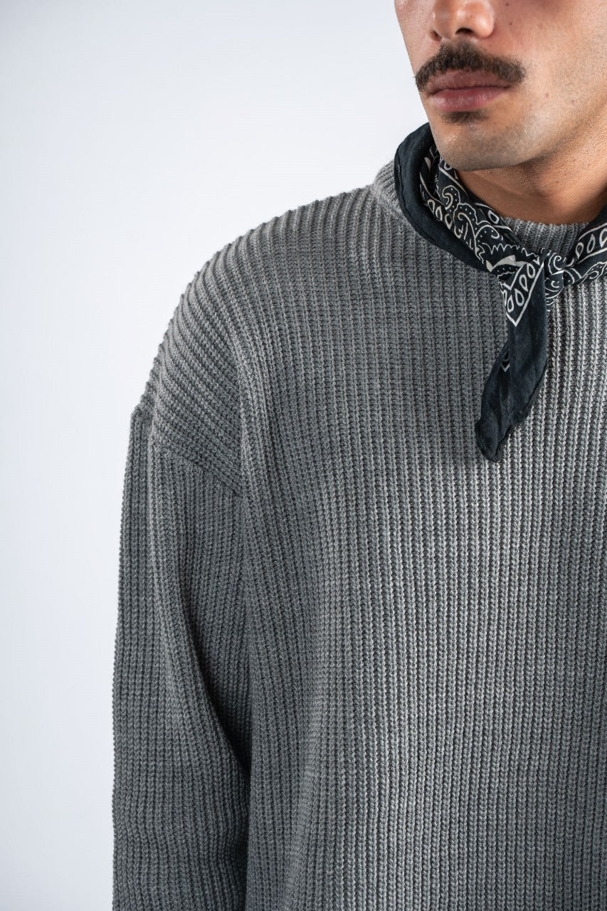 Person wearing a gray ribbed sweater with a black bandana around the neck on a light gray background