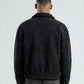 Person wearing a dark textured jacket and jeans on a white background