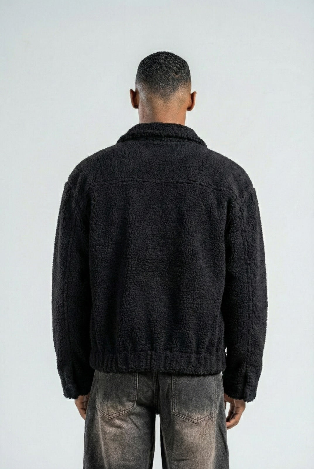 Person wearing a dark textured jacket and jeans on a white background