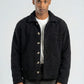 Man wearing a dark jacket over a white shirt on a plain background