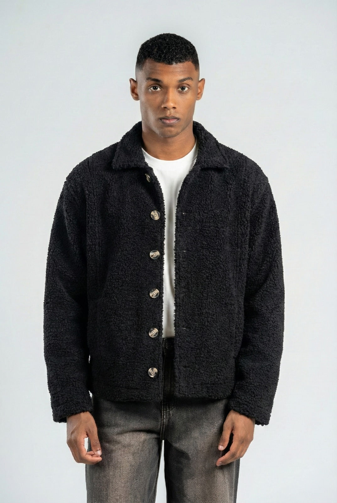 Man wearing a dark jacket over a white shirt on a plain background