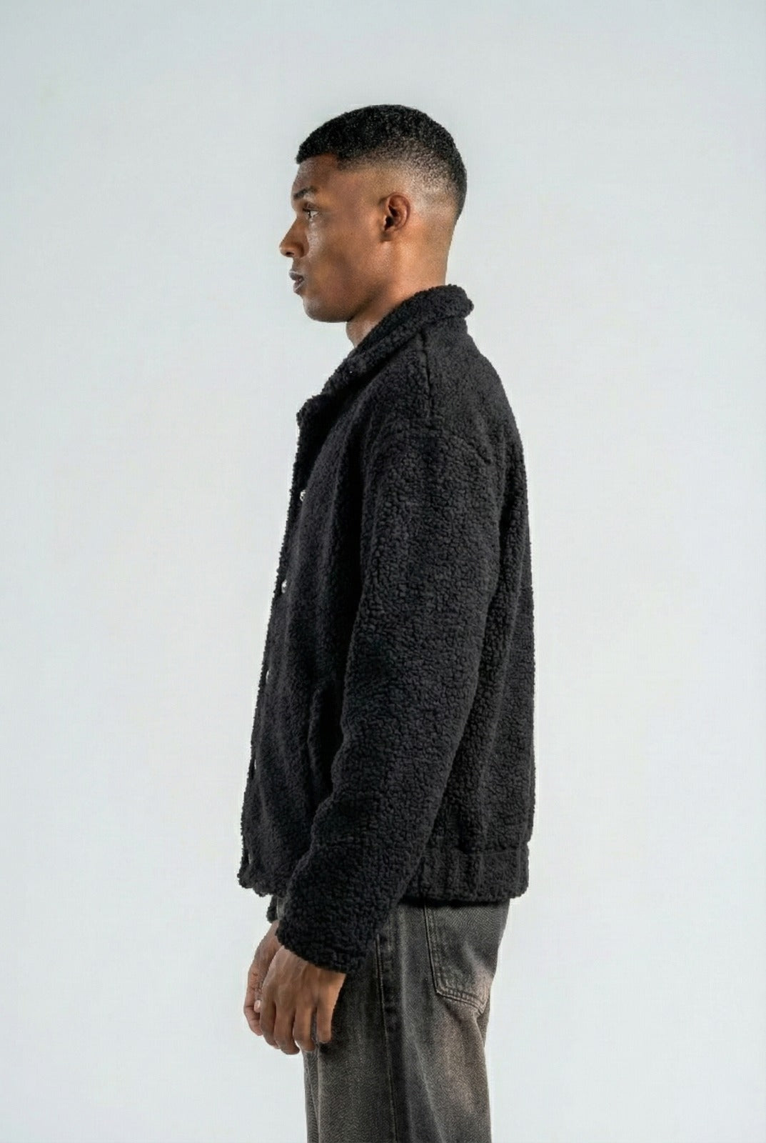 Man wearing a dark jacket and gray pants against a white background