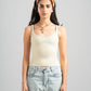 Woman wearing a beige tank top and light blue jeans against a gray background