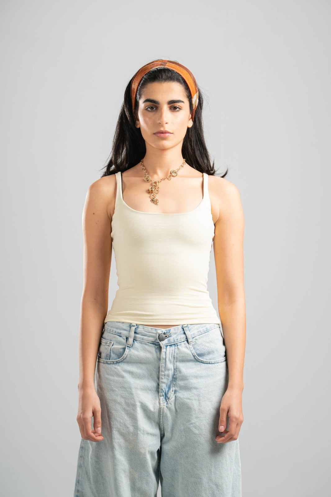 Woman wearing a beige tank top and light blue jeans against a gray background