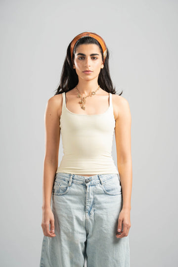 Woman wearing a beige tank top and light blue jeans against a gray background