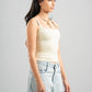 Woman wearing a beige tank top and light blue jeans against a gray background