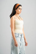Woman wearing a beige tank top and light blue jeans against a gray background