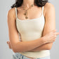 Woman wearing a beige tank top and light blue jeans with a gold necklace on a gray background