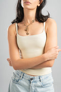 Woman wearing a beige tank top and light blue jeans with a gold necklace on a gray background