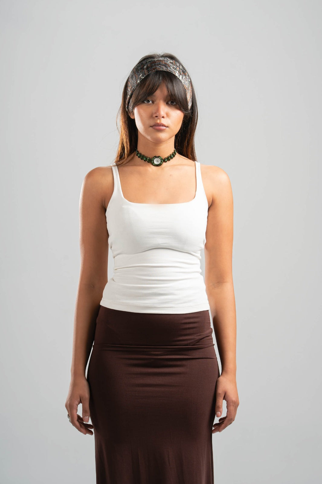 Woman wearing a white tank top and brown skirt on a gray background
