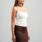 Woman wearing a white tank top and brown skirt on a gray background