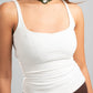 Woman wearing a white tank top and brown skirt with a green necklace on a gray background