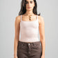 Woman wearing a light pink tank top and brown pants against a gray background