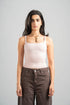 Woman wearing a light pink tank top and brown pants against a gray background