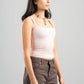 Woman wearing a light pink tank top and brown pants on a gray background