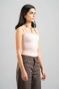 Woman wearing a light pink tank top and brown pants on a gray background
