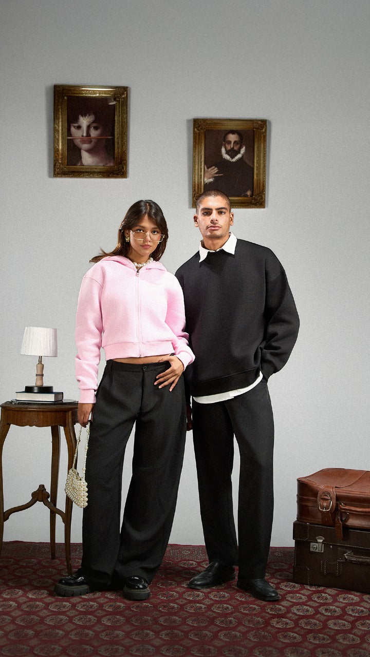 Two people standing in a room with framed pictures on the wall and a table with a lamp.