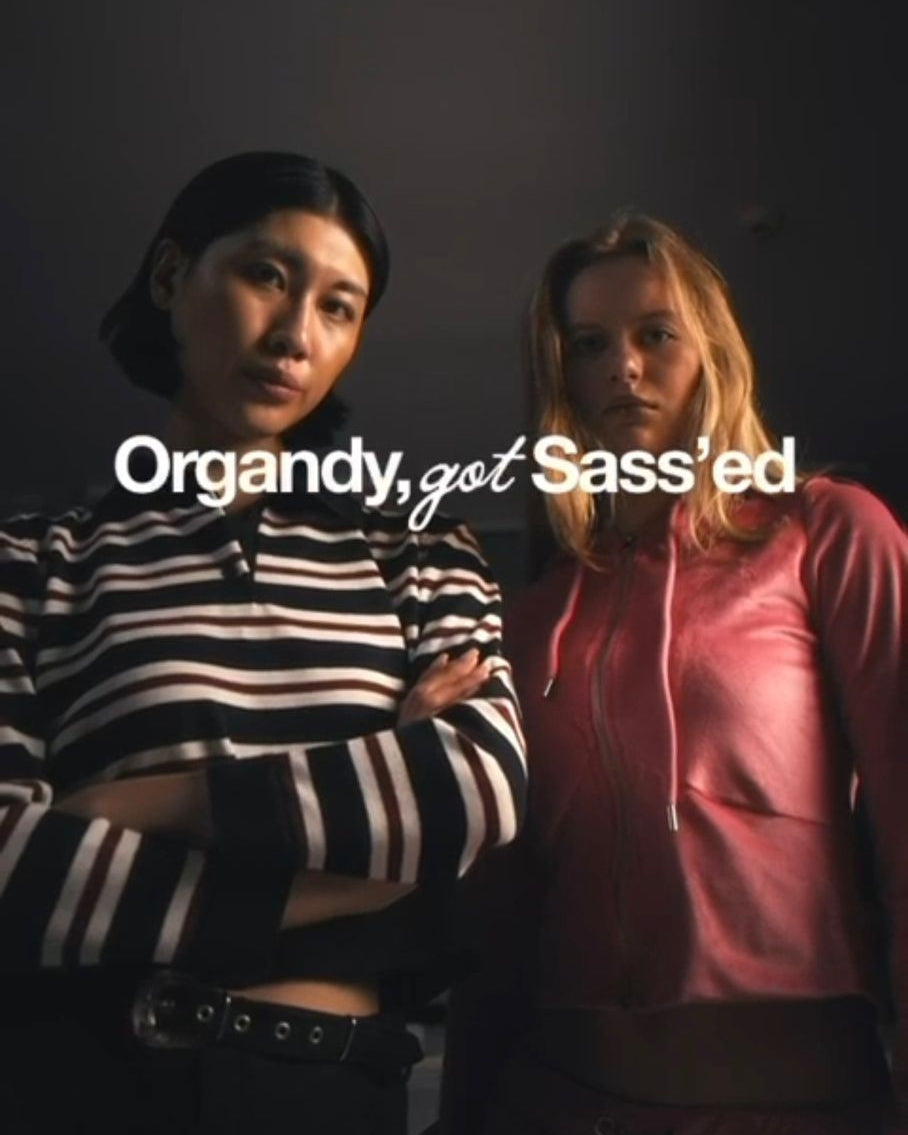 Two people standing side by side with text overlay 'Organdy, got Sass'ed' on a dark background
